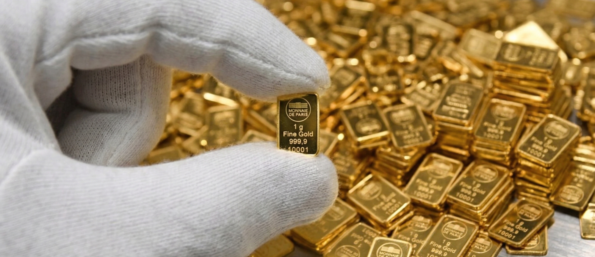 Eine Hand hält einen goldenen Barren, umgeben von weiteren Goldbarren.