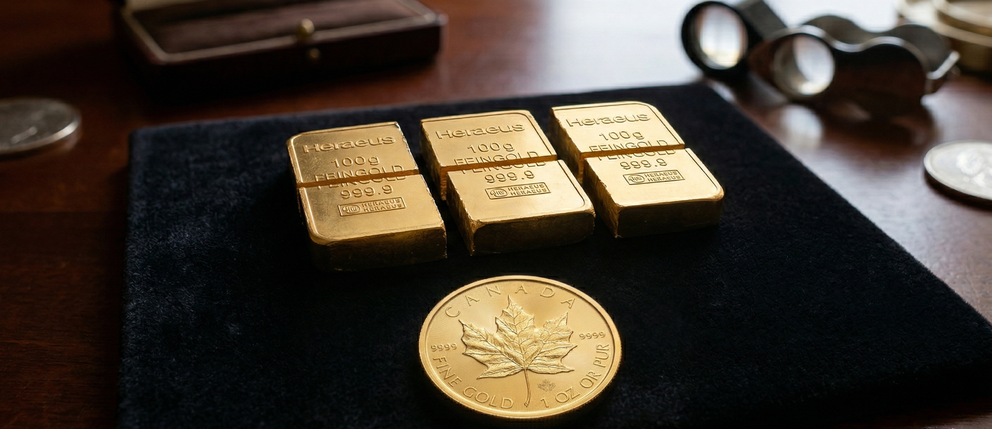 Vier Goldbarren und eine goldene Münze auf einem samtigen Untergrund.